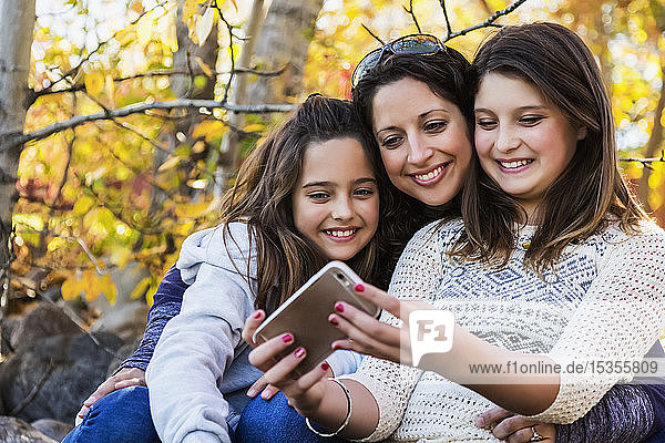 A mom and her two daughters taking a self-portrait while resting during a family outing in a city park on a warm fall day; Edmonton  Alberta  Canada