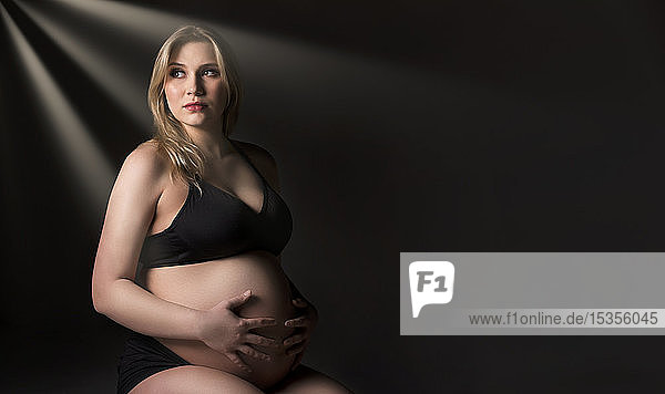 Eine junge schwangere Frau  die in einem Studio ihren Bauch hält und von der Kamera wegschaut  denkt an ihr ungeborenes Kind: Edmonton  Alberta  Kanada
