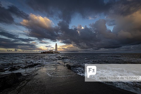 Leuchtturm  St. Mary's Lighthouse mit überspülter Straße bei Flut mit dramatischen Wolken bei Sonnenuntergang  Küste von Tyne  Northumberland  Großbritannien