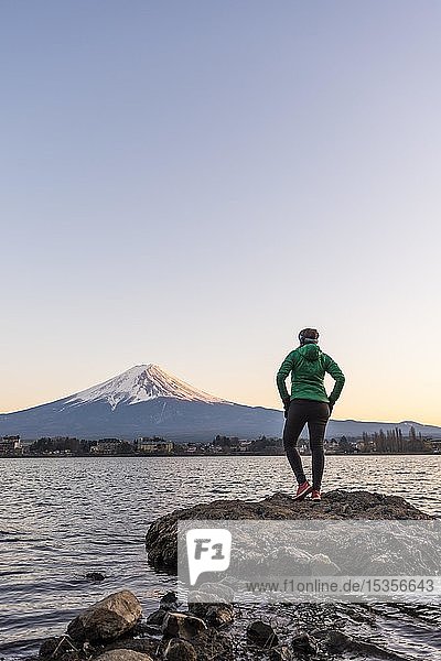 Evening mood  Young woman standing on a stone in the water and looking into the distance  view over Lake Kawaguchi  back volcano Mt. Fuji  Yamanashi Prefecture  Japan  Asia