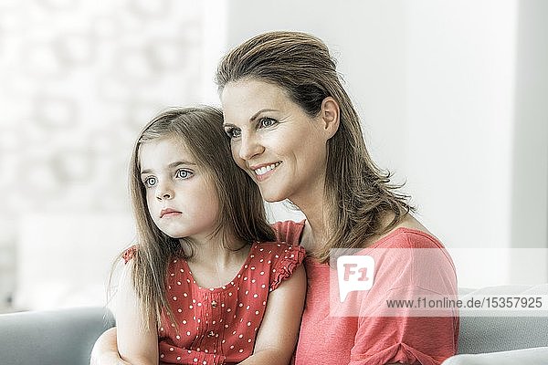 Mother and daughter sit together on the couch and look into the distance  smile  Germany  Europe