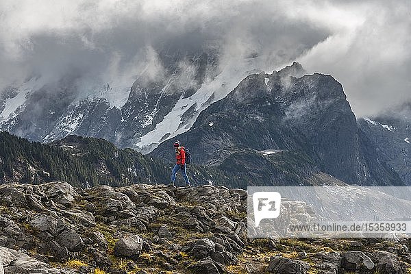 Female hiker off Mt. Shuksan with snow and glacier in cloudy sky  Mt. Baker-Snoqualmie National Forest  Washington  USA  North America