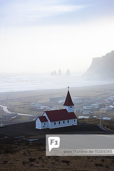Kleine Kirche mit rotem Dach  dahinter das Dorf Vik und die Felsen von Reynisfjara  Sudurland  Südisland  Island  Europa