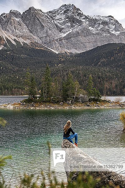 Young woman sitting on a rock on the shore  view into the distance  Eibsee lake in front of Zugspitzmassiv with Zugspitze  Wetterstein range  near Grainau  Upper Bavaria  Bavaria  Germany  Europe