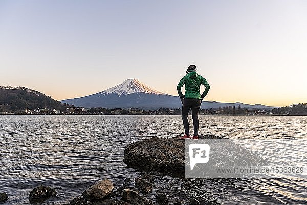 Evening mood  Young woman standing on a stone in the water and looking into the distance  view over Lake Kawaguchi  back volcano Mt. Fuji  Yamanashi Prefecture  Japan  Asia
