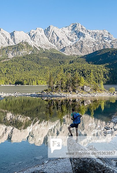 Hiker standing on rocks  view into the distance  Zugspitze and Wetterstein range with reflection in the Eibsee lake  near Grainau  Upper Bavaria  Bavaria  Germany  Europe