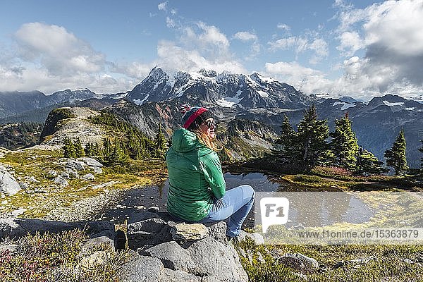 Wanderin  die sich auf einem Felsen an einem kleinen Bergsee ausruht  Blick vom Tabletop Mountain zum Mt. Shuksan mit Schnee und Gletscher  Mt. Baker-Snoqualmie National Forest  Washington  USA  Nordamerika