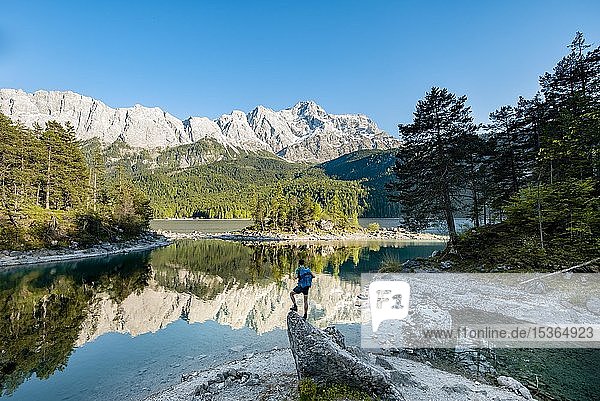 Hiker standing on rocks  view into the distance  Zugspitze and Wetterstein range with reflection in the Eibsee lake  near Grainau  Upper Bavaria  Bavaria  Germany  Europe