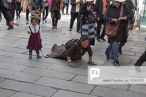 Pilger mit Kind  der eine Strecke läuft und sich dann niederwirft  umrundet den Jokhang-Tempel in Lhasa  Tibet  China  Asien