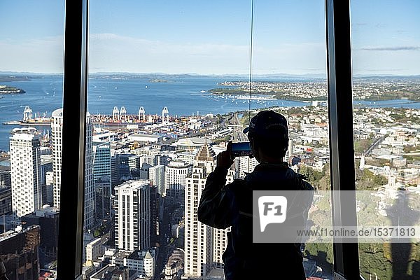 Tourist fotografiert die Aussicht mit seinem Smartphone,  Sky Tower Aussichtsplattform,  Skyline mit Wolkenkratzern,  Central Business District,  Auckland,  Nordinsel,  Neuseeland,  Ozeanien