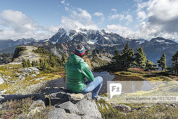 Female hiker resting on a rock at a small mountain lake  view from Tabletop Mountain to Mt. Shuksan with snow and glacier  Mt. Baker-Snoqualmie National Forest  Washington  USA  North America