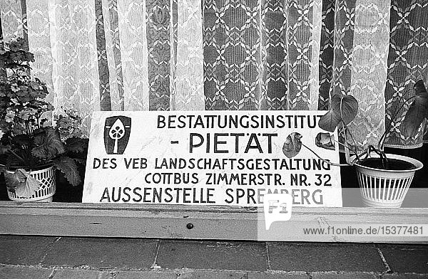 Schaufenster des Bestattungsinstituts PIETÄT Filiale Sprember mit Firmenschild  Vorhang und Grünpflanze  Bezirk Cottbus  Stadt Spremberg  DDR  Deutschland  Europa