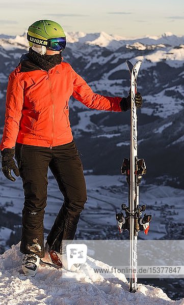 Skifahrerin mit Skihelm stehend mit Ski an der Skipiste oberhalb des Tals  Blick zur Seite  Berge dahinter  SkiWelt Wilder Kaiser  Brixen im Thale  Tirol  Österreich  Europa