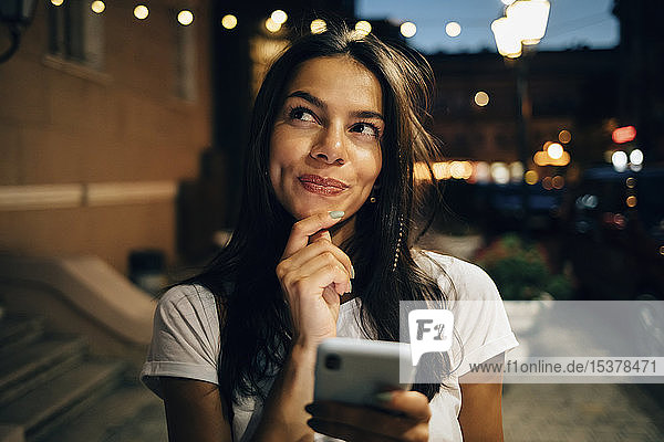 Young woman using smartphone in the city at night  looking up