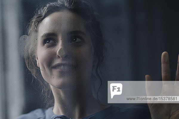 Profil einer lächelnden jungen Frau hinter einer Fensterscheibe