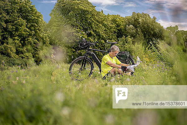 Ein reifer Mann  der während seiner Fahrradtour mit dem Elektrofahrrad eine Pause macht und auf eine Karte schaut