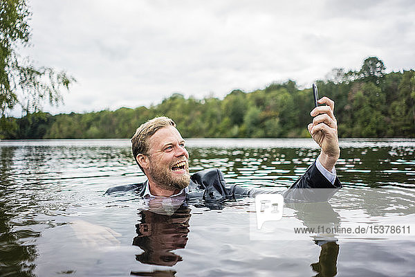 Verrückter Geschäftsmann hält Handy in einem See