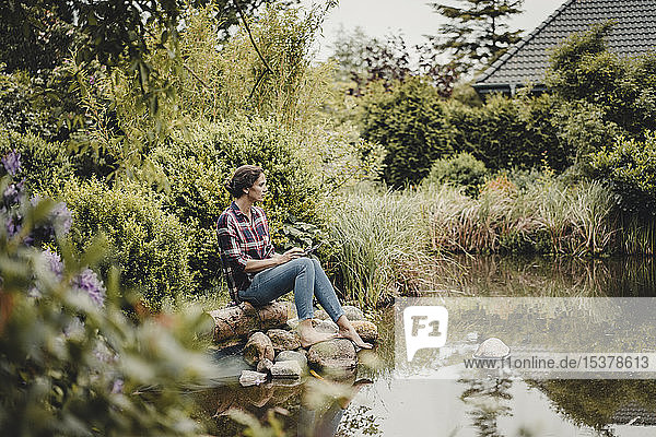 Woman sitting at garden pond  using digital tablet