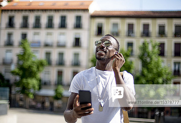 Smiling young man using smartphone and ear phones  looking up