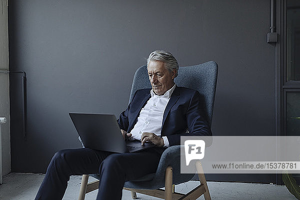 Leitender Geschäftsmann im Sessel sitzend mit Laptop