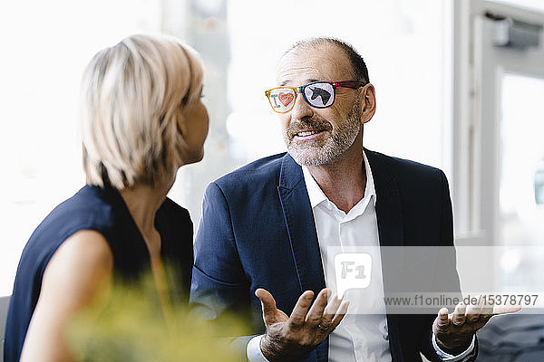 Geschäftsmann mit Einhornbrille  spricht mit Geschäftsfrau