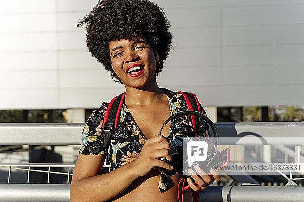 Lächelnde afro-amerikanische Frau mit rotem Smartphone und Kopfhörern