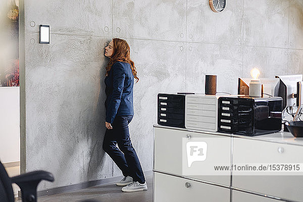 Müde Geschäftsfrau lehnt im Büro gegen eine Wand