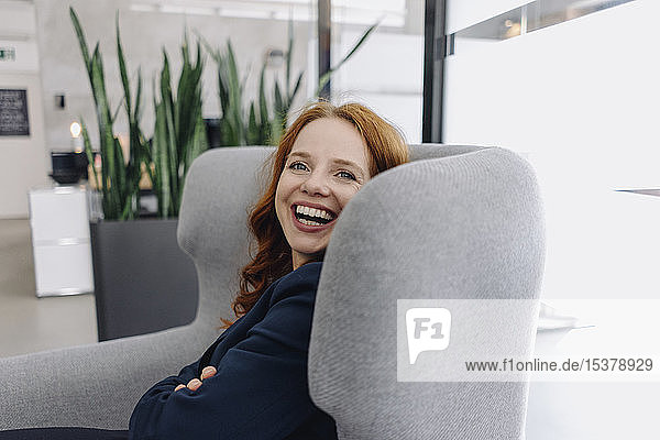 Glückliche rothaarige Geschäftsfrau im Sessel sitzend