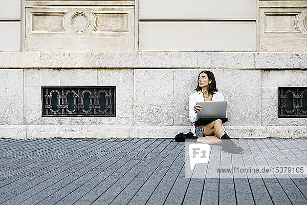 Geschäftsfrau  die in der Stadt am Boden sitzt und einen Laptop benutzt