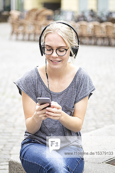 Porträt einer blonden Frau mit Smartphone und Kopfhörer