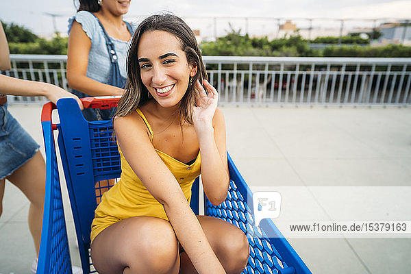 Porträt einer lächelnden jungen Frau mit Freunden in einem Einkaufswagen