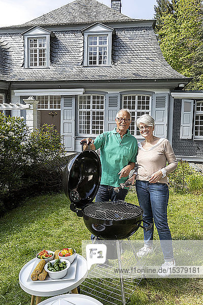 Glückliches älteres Ehepaar beim Grillen im Garten ihres Hauses