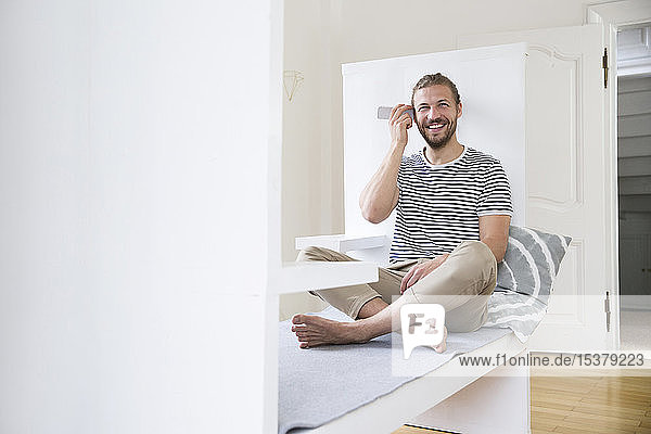 Lächelnder junger Mann benutzt Smartphone zu Hause