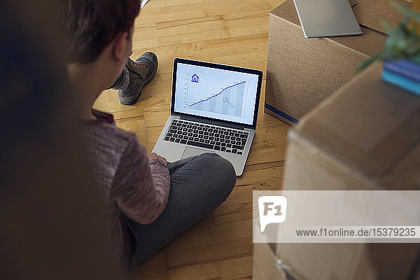 Frau mit Laptop mit aufsteigender Liniengrafik auf dem Bildschirm in einem neuen Zuhause