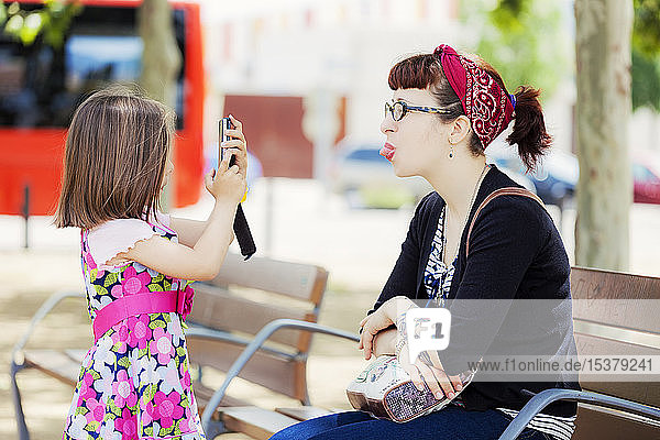 Little girl taking photo of her mother with smartphone