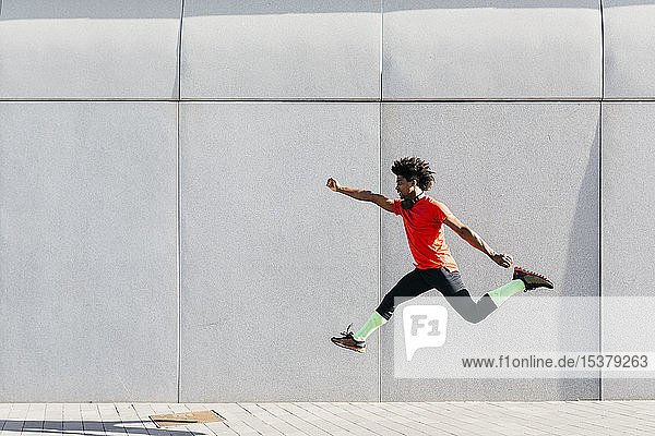 Young man doing jumps with a gray wall in the background
