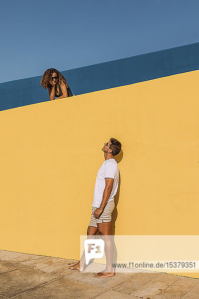 Junger Mann sieht Frau hinter einer gelben Wand an