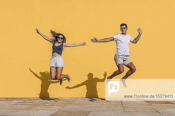 Junges Paar springt vor eine gelbe Mauer