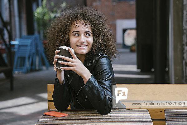 Porträt einer lächelnden Teenagerin  die auf einer Bank sitzt und Kaffee zum Mitnehmen