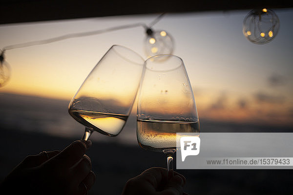 Woman holding two glasses of white wine in van at sunset