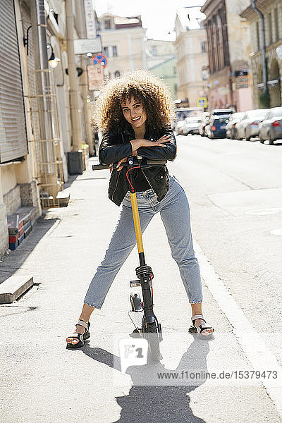 Porträt eines lächelnden Teenager-Mädchens  das mit einem Roller auf dem Bürgersteig steht