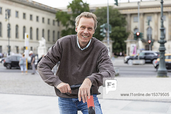 Porträt eines glücklichen älteren Mannes  der sich auf einen Elektroroller stützt  in der Stadt  Berlin  Deutschland