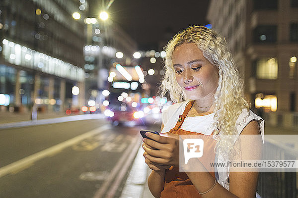 Young woman in London at night looking at her smartphone
