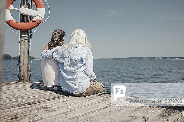 Mutter und Tochter schauen auf das Meer  auf dem Steg sitzend  Rückansicht
