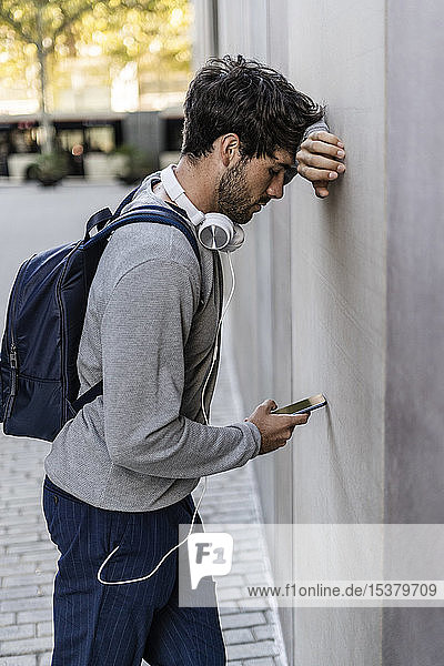 Mann lehnt gegen eine Wand und überprüft Handy
