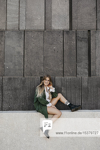 Portrait of blond young woman wearing green jacket sitting on a wall  Vienna  Austria