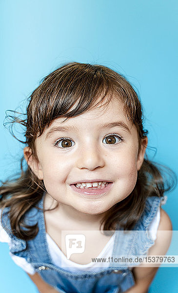 Porträt eines niedlichen kleinen Mädchens  das sehr ausdrucksstark lächelt  auf blauem Hintergrund