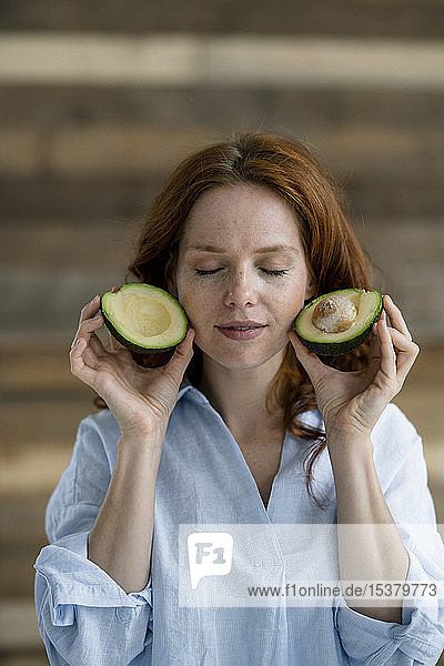 Porträt einer rothaarigen Frau mit geschlossenen Augen  die eine in Scheiben geschnittene Avocado hält