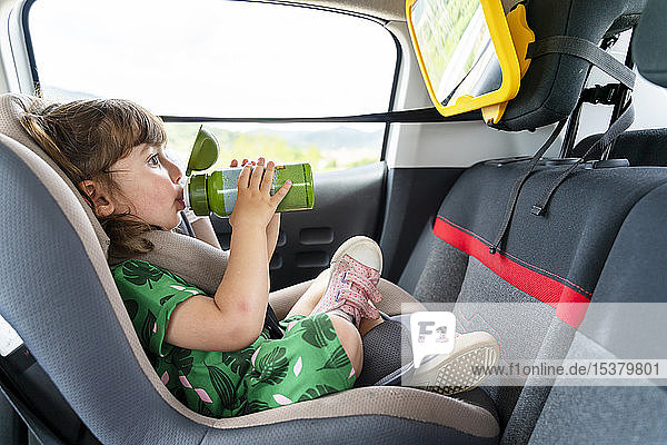 Toddler girl sitting on a car seat with a mirror drinking water