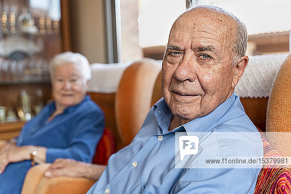 Älterer Mann mit seiner Frau auf einem Sessel im Wohnzimmer sitzend